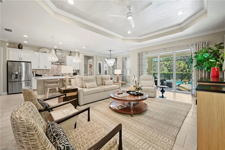 Living room with ornamental molding, a tray ceiling, recessed lighting, a ceiling fan, and a chandelier