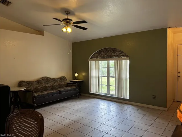 Living room with ceiling fan, light tile patterned floors, and vaulted ceiling