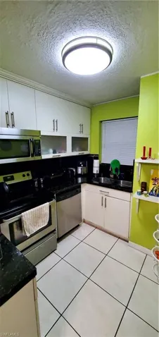 Kitchen with a textured ceiling, dishwasher, range, and white cabinetry