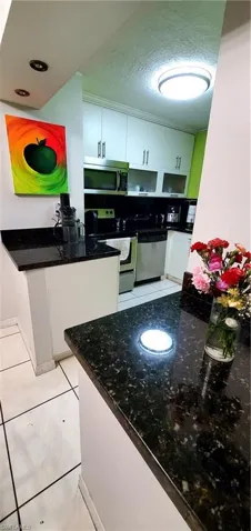 Kitchen featuring dishwashing machine, white cabinetry, light tile patterned floors, and stainless steel range with electric cooktop