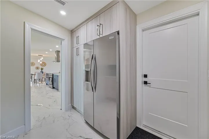 Kitchen featuring stainless steel appliances, light marble finish floors, wall chimney exhaust hood, modern cabinets, and recessed lighting