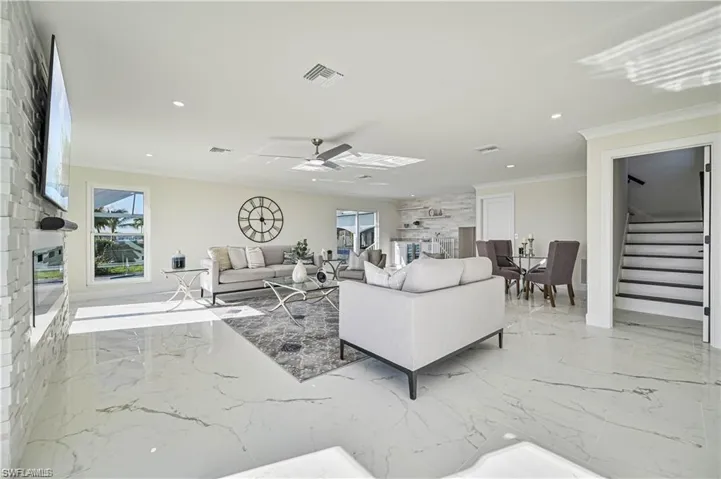 Living room with stairway, marble tiled flooring, ornamental molding, a fireplace, and ceiling fan