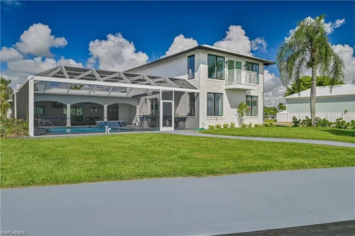 Back of house featuring stucco siding, an outdoor pool, a balcony, a lawn, and a lanai