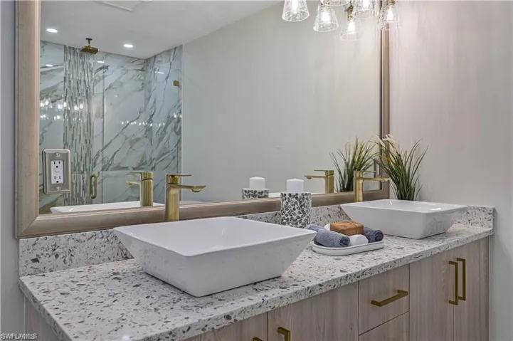 Bathroom with double vanity, a marble finish shower, and a chandelier