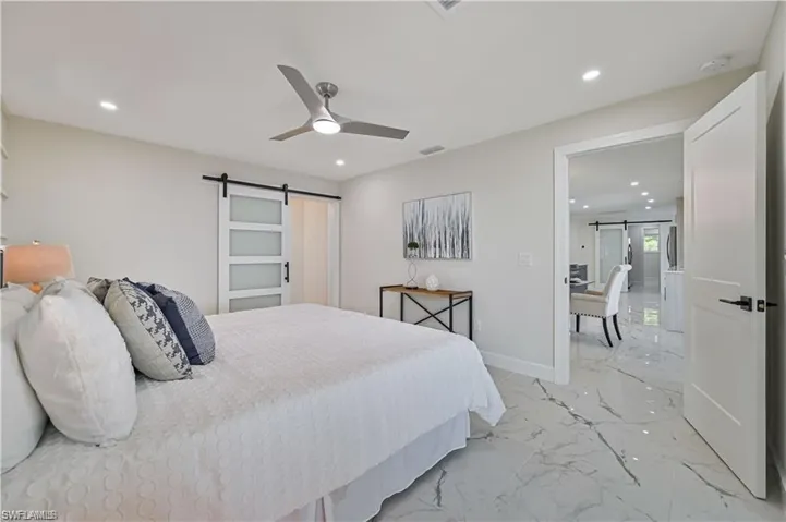 Bedroom with a barn door, light marble finish flooring, recessed lighting, and ceiling fan