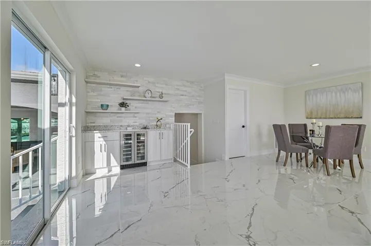 Dining space with wine cooler, recessed lighting, a bar, crown molding, and light marble finish flooring