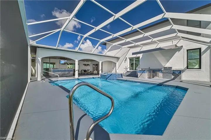 View of pool with an outdoor kitchen, a patio area, a pool with connected hot tub, and glass enclosure