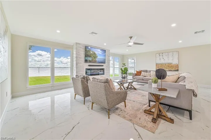Living room featuring marble tiled floors, plenty of natural light, a fireplace, ornamental molding, and recessed lighting