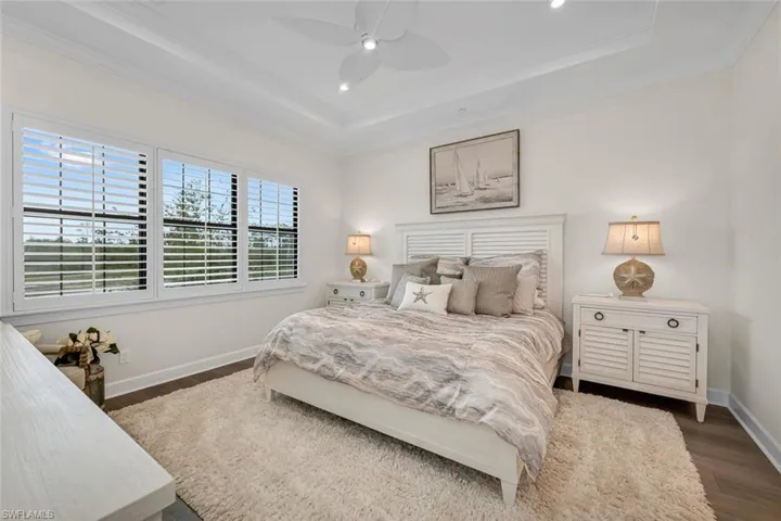 Bedroom featuring dark wood-type flooring, ceiling fan, baseboards, a tray ceiling, and ornamental molding