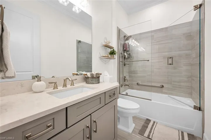 Full bathroom featuring bath / shower combo with glass door, toilet, ornamental molding, and vanity