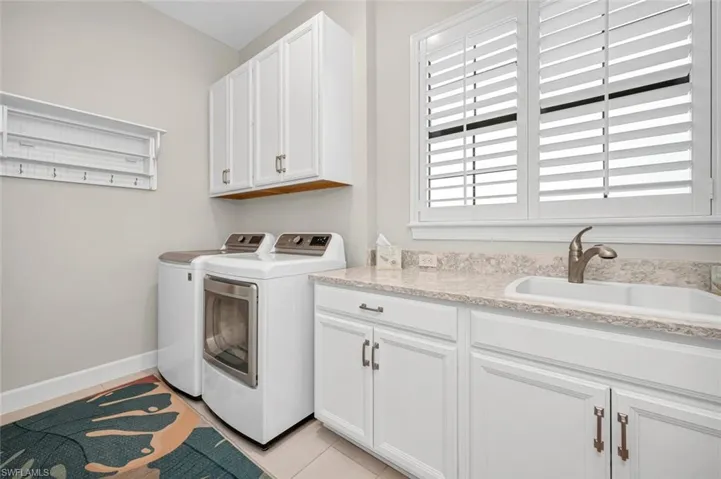 Washroom with baseboards, separate washer and dryer, light tile patterned flooring, cabinet space, and a sink