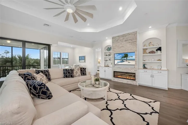 Living room with visible vents, ornamental molding, built in features, a tray ceiling, and wood finished floors