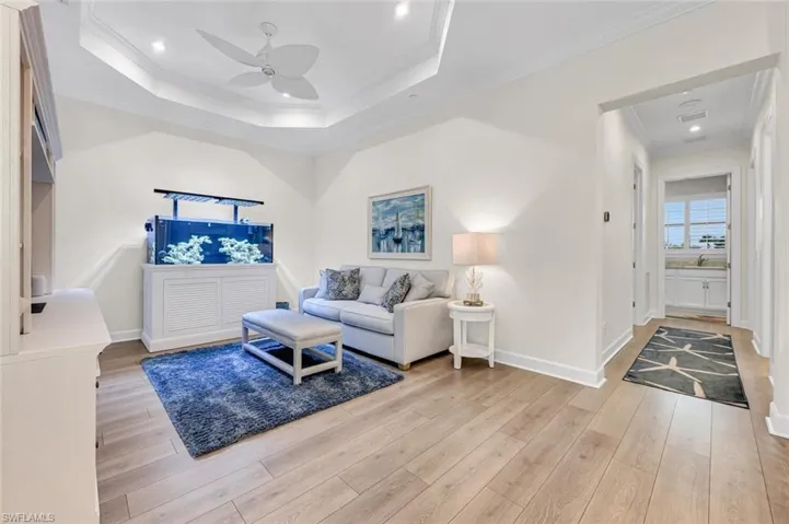 Living area featuring a ceiling fan, baseboards, ornamental molding, a raised ceiling, and light wood-type flooring