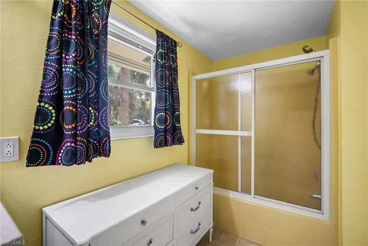 Bathroom with tile flooring, a textured ceiling, combined bath / shower with glass door, and vanity