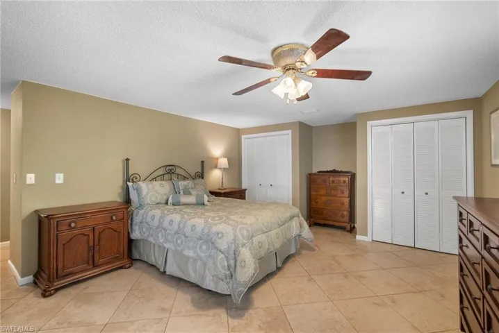 Tiled bedroom featuring a textured ceiling, ceiling fan, and multiple closets