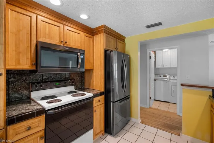 Kitchen with tasteful backsplash, light wood-type flooring, washing machine and dryer, appliances with stainless steel finishes, and a textured ceiling