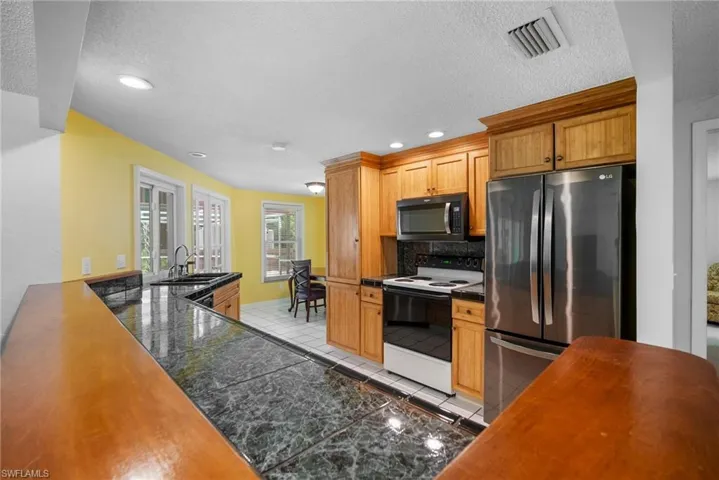 Kitchen featuring a textured ceiling, stainless steel appliances, backsplash, sink, and light tile floors