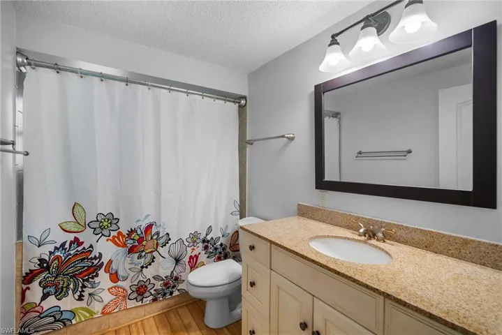 Bathroom featuring wood-type flooring, oversized vanity, toilet, and a textured ceiling