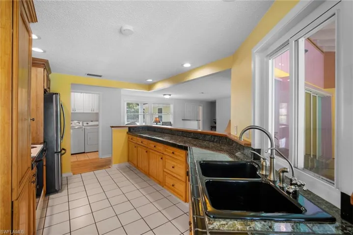 Kitchen featuring washing machine and clothes dryer, kitchen peninsula, stainless steel fridge, light tile floors, and sink