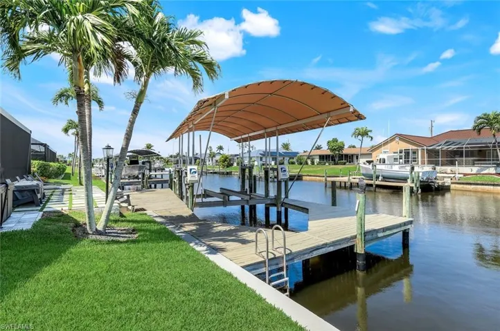 Dock featuring boat lift, a water view, a lawn, and a residential view