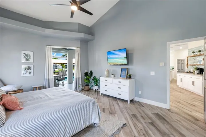 Bedroom with access to outside, light wood-type flooring, high vaulted ceiling, baseboards, and ceiling fan