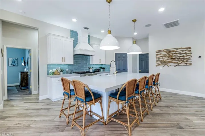 Kitchen featuring light countertops, premium range hood, a kitchen island with sink, a breakfast bar, and recessed lighting