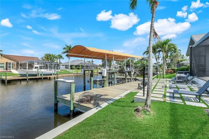 Dock with boat lift, a water view, a lawn, and a residential view