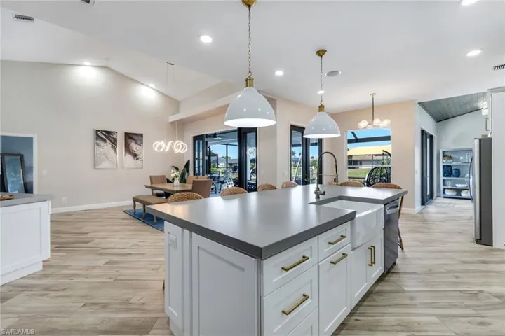 Kitchen with stainless steel appliances, a sink, light wood-style flooring, dark countertops, and an island with sink
