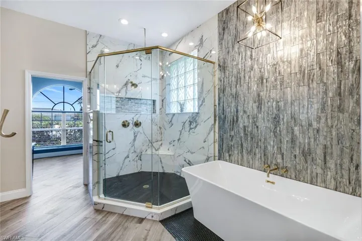 Bathroom with a freestanding tub, wood finished floors, a marble finish shower, a chandelier, and recessed lighting