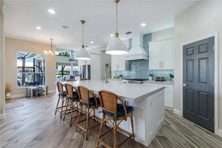 Kitchen featuring stainless steel refrigerator with ice dispenser, a sink, a large island, premium range hood, and light countertops