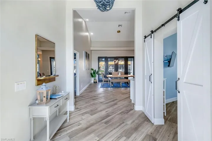 Hallway with a barn door, light wood finished floors, baseboards, high vaulted ceiling, and french doors