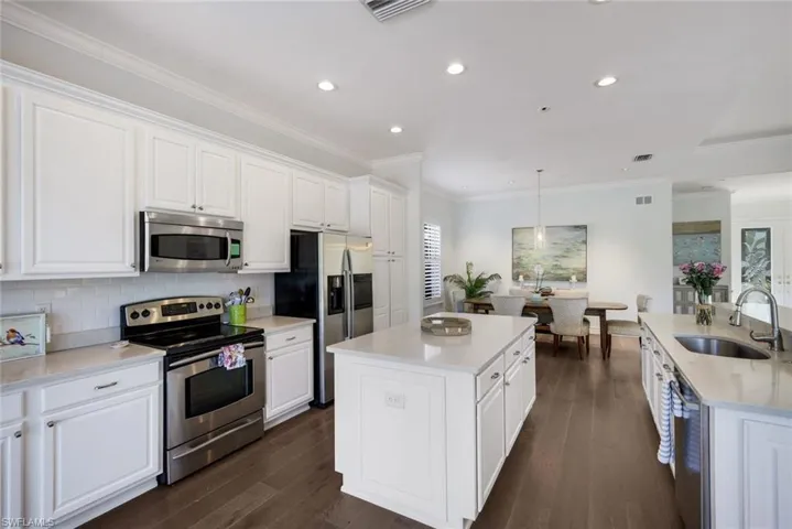 Kitchen with stainless steel appliances, white cabinets, light stone countertops, hanging light fixtures, and ornamental molding