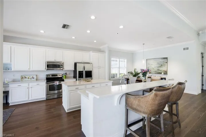 Kitchen with stainless steel appliances, pendant lighting, dark wood-style floors, a kitchen bar, and crown molding