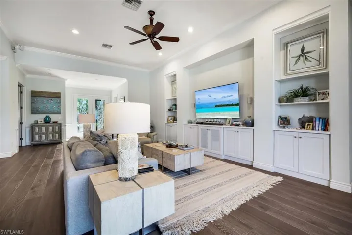 Living room with built in features, dark wood-style flooring, ceiling fan, crown molding, and recessed lighting