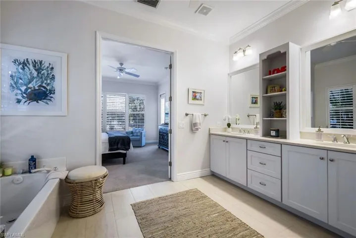 Ensuite bathroom featuring crown molding, double vanity, a garden tub, and ceiling fan