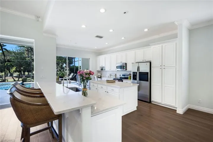 Kitchen featuring white cabinets, stainless steel appliances, a breakfast bar area, dark wood finished floors, and a kitchen island with sink