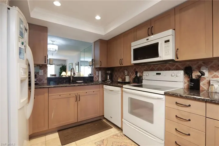 Kitchen featuring white appliances, decorative backsplash, dark stone counters, recessed lighting, and a raised ceiling