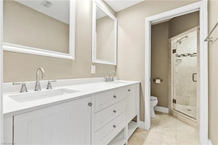 Full bath with double vanity, a stall shower, and light tile patterned flooring