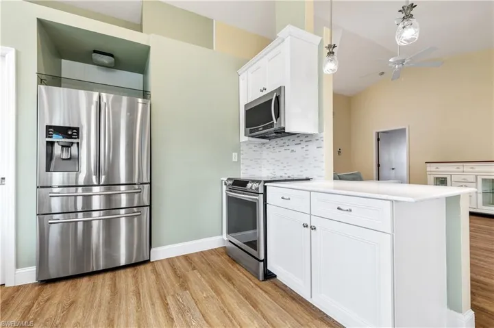 Kitchen featuring stainless steel appliances, white cabinets, a peninsula, a ceiling fan, and light wood-style flooring