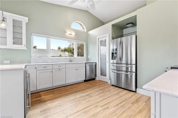 Kitchen with stainless steel appliances, glass insert cabinets, white cabinets, lofted ceiling, and light wood finished floors