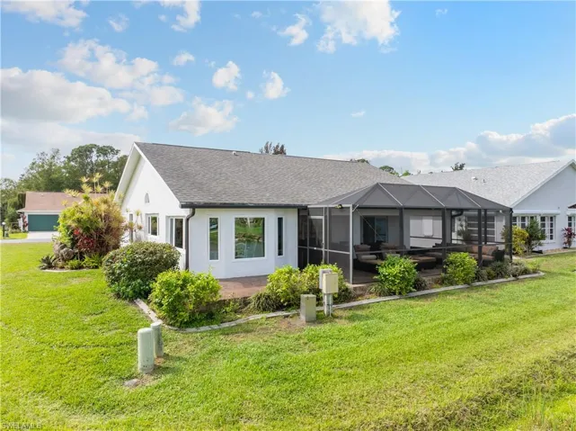 Rear view of property featuring a sunroom, a lawn, a lanai, a shingled roof, and stucco siding