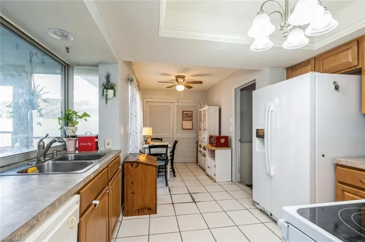 Kitchen featuring a tray ceiling, ceiling fan with notable chandelier, pendant lighting, white appliances, and sink