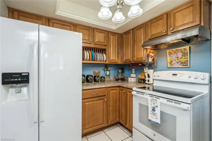 Kitchen with a chandelier, white appliances, ornamental molding, a raised ceiling, and light tile patterned floors