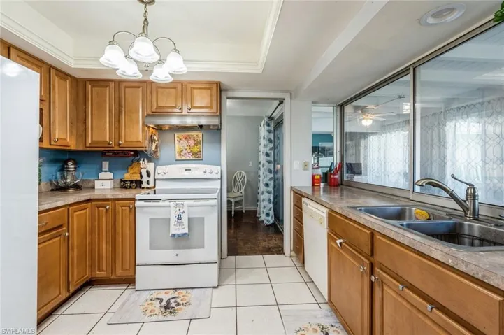 Kitchen featuring white appliances, pendant lighting, light tile patterned floors, ceiling fan with notable chandelier, and a raised ceiling