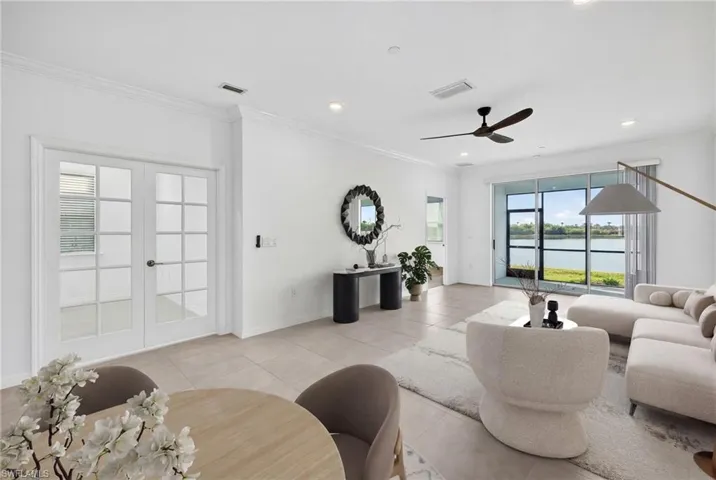 Living area featuring crown molding, french doors, light tile patterned floors, a ceiling fan, and a water view