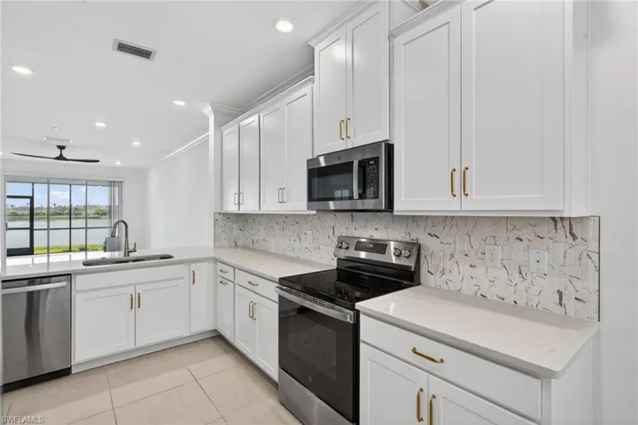 Kitchen with stainless steel appliances, white cabinets, decorative backsplash, ceiling fan, and light tile patterned floors