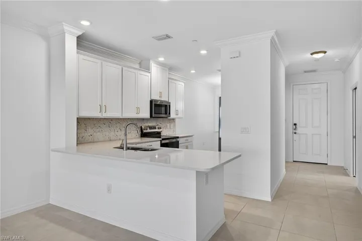 Kitchen featuring a peninsula, stainless steel appliances, decorative backsplash, white cabinets, and light stone counters