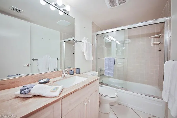 Full bathroom with bath / shower combo with glass door, light tile patterned floors, and vanity