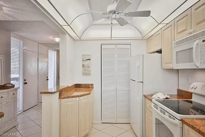 Kitchen featuring white appliances, light tile patterned floors, a ceiling fan, a peninsula, and a textured ceiling