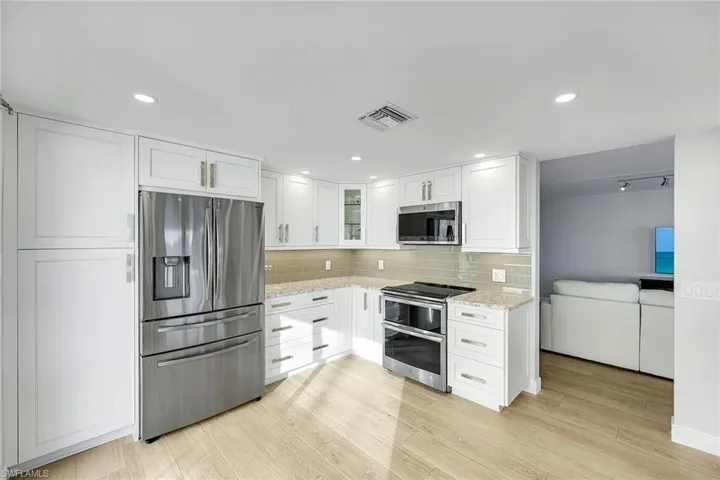 Kitchen featuring stainless steel appliances, white cabinets, light stone counters, light wood-style floors, and glass insert cabinets